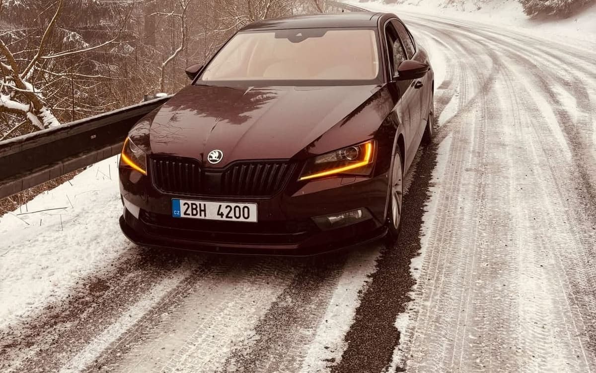 Vínová Škoda Superb na zasněžené silnici v Jizerských horách